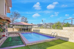 A swimming pool with a small deck area, a covered seating area, and a view of the surrounding buildings. - Collection O Gold Valley (Lonavala)
