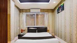 A hotel room with a bed, a nightstand, a window, and a wall with patterned wallpaper. - Collection O Gold Valley (Lonavala)