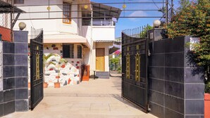 A gated entrance to a property with a stone wall, potted plants, and a clear sky. - Collection O Gold Valley (Lonavala)