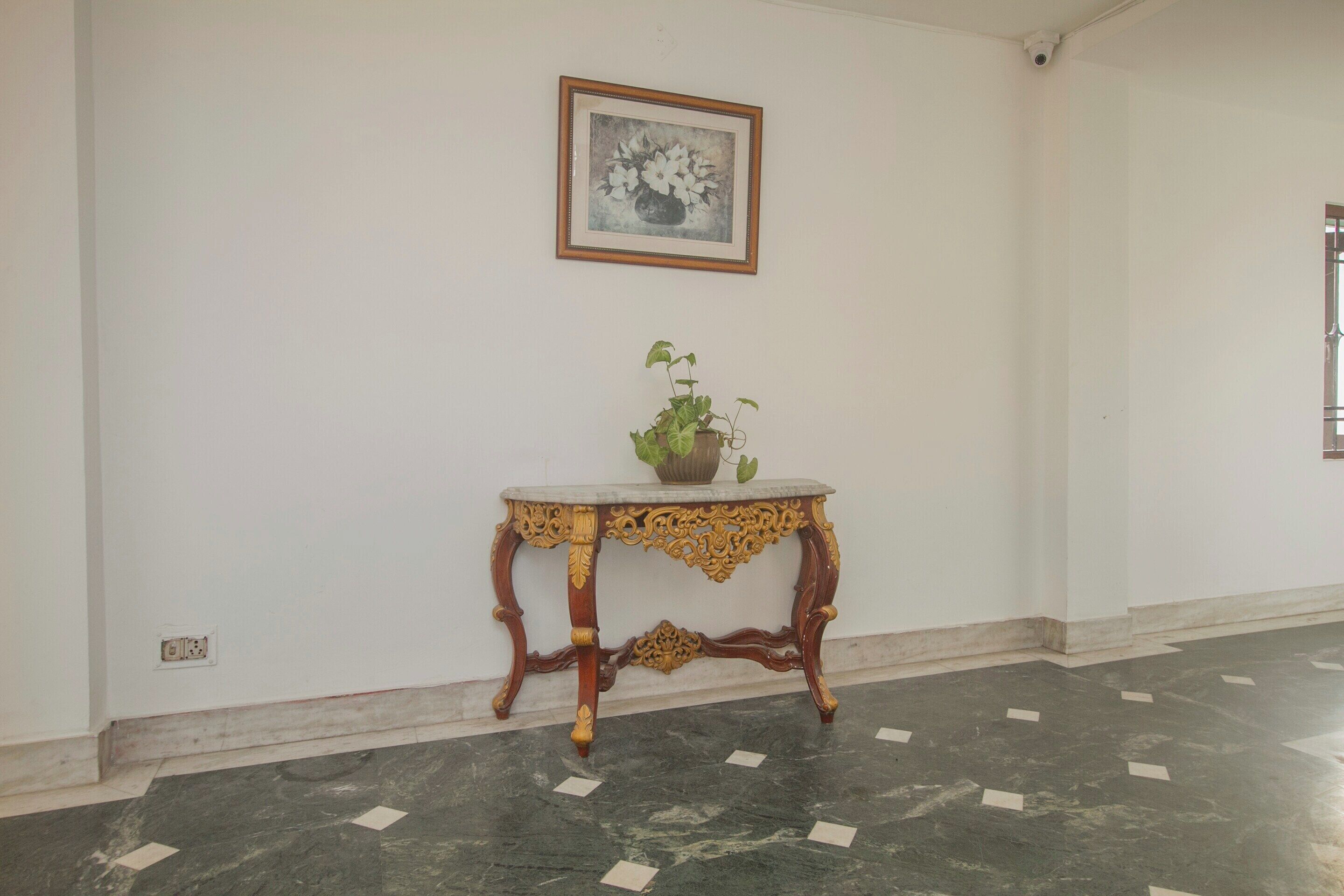 Una habitación con piso de mármol, una mesa decorativa con una planta y un cuadro en la pared.