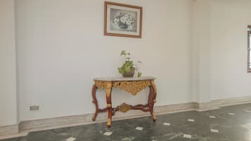 Una habitación con piso de mármol, una mesa decorativa con una planta y un cuadro en la pared.