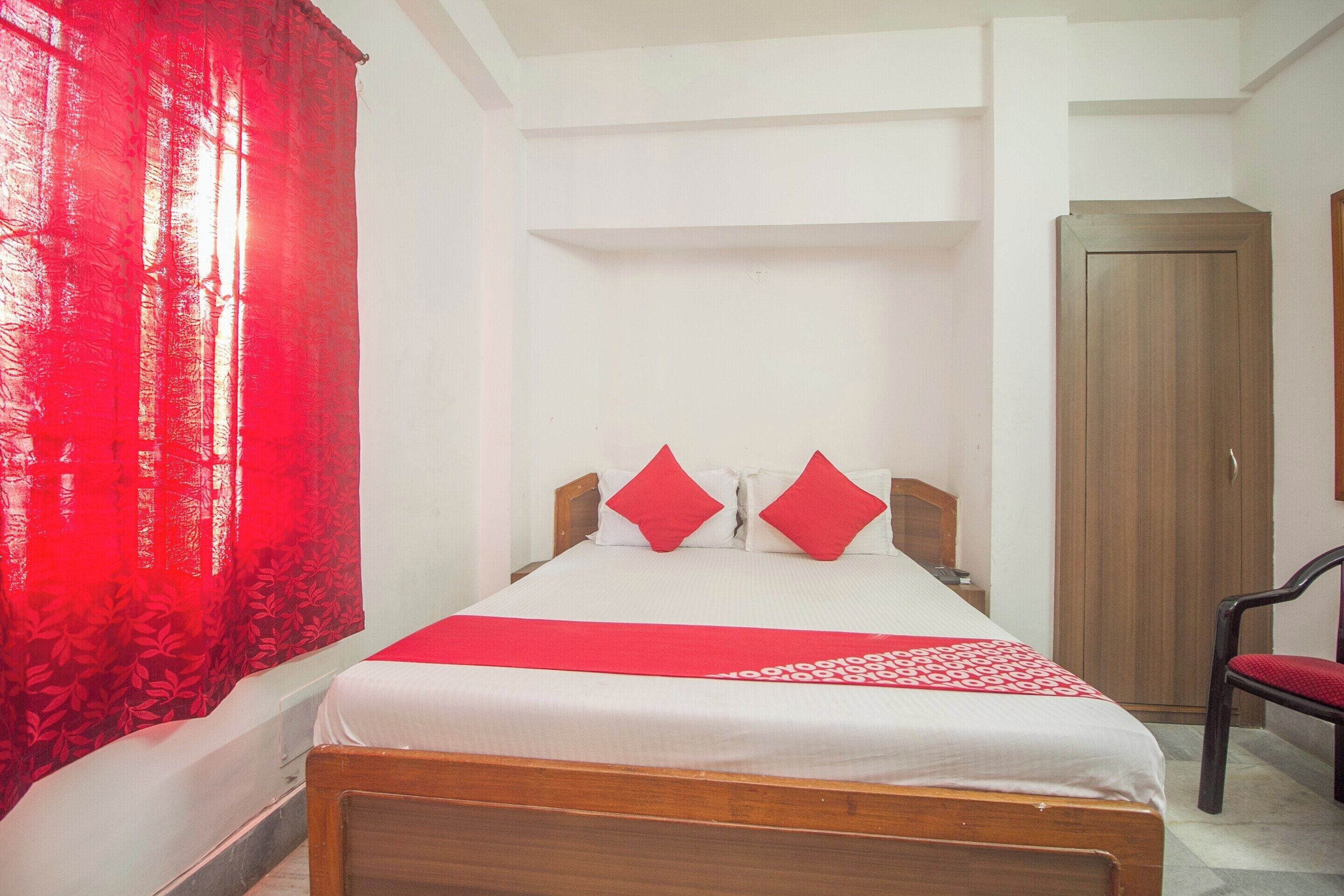 A hotel room with a bed, a chair, a wardrobe, and a red curtain.
