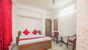 A bedroom with a wooden bed, red pillows, a small table with chairs, and a mirror on the wall. - Collection O Sevoke Crossway Siliguri (Siliguri)