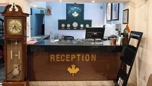 A reception desk with a clock, a framed sign with a maple leaf, and a flag. - Collection O Sevoke Crossway Siliguri (Siliguri)