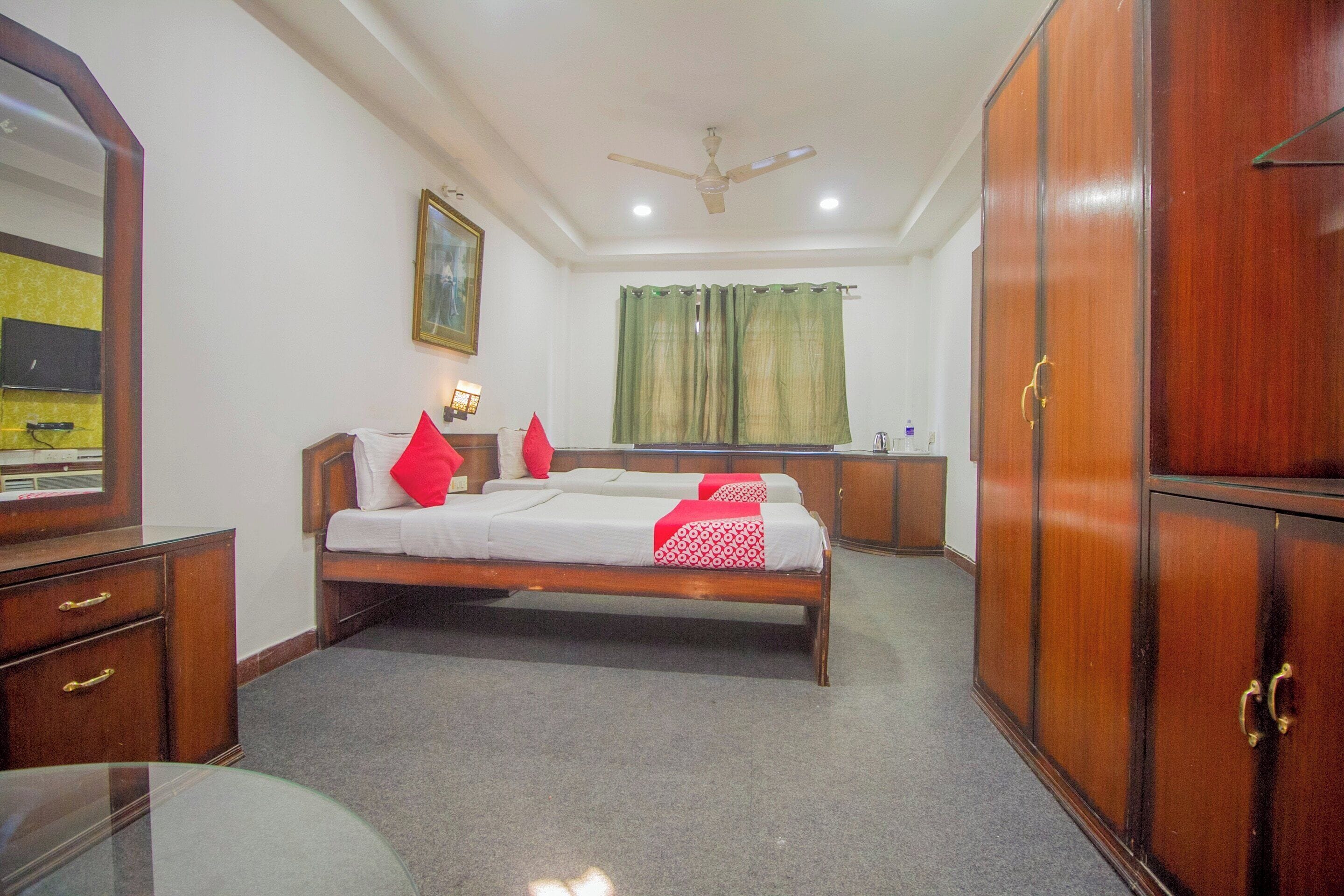 A hotel room with a bed, a desk, a wardrobe, a ceiling fan, and a window with curtains.