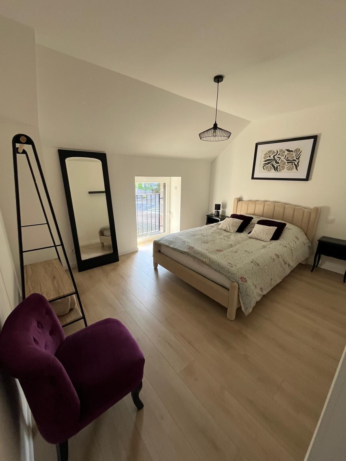 A bedroom with a bed, a chair, a ladder, a mirror, a picture on the wall, and a door leading to a balcony.