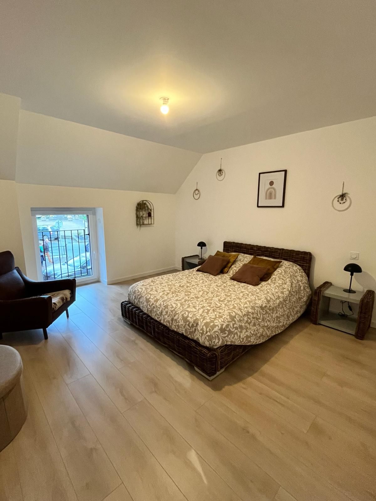 A bedroom with a large bed, a chair, a small table, and a window with a view of the outside.