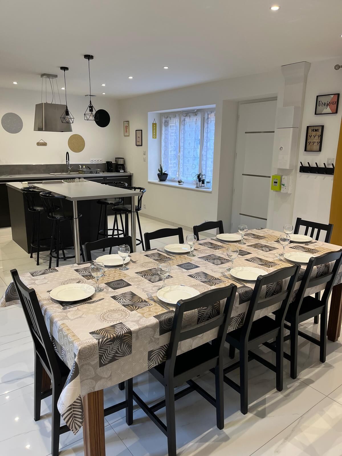 Een moderne keuken met een centraal eiland, een eettafel gedekt voor zes personen en een raam met gordijnen.