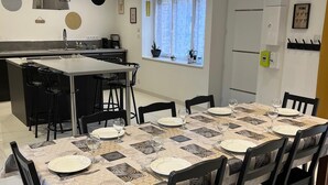 Ett modernt kök med en central köksö, ett matbord med plats för sex personer och ett fönster med gardiner.