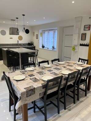 Een moderne keuken met een centraal eiland, een eettafel gedekt voor zes personen en een raam met gordijnen.