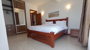 A bedroom with a wooden bed, a wardrobe, a bedside table, and a painting on the wall. - Myra Residence (Nairobi)