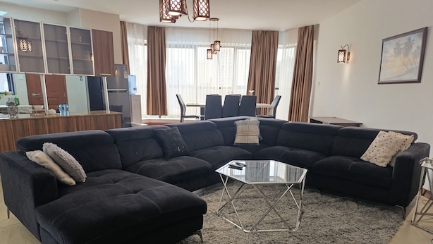 A living room with a sectional sofa, a glass coffee table, and a rug. - Myra Residence (Nairobi)