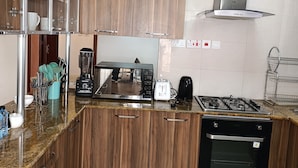 A modern kitchen with wooden cabinets, a stainless steel range hood, a built-in microwave, and a dishwasher. - Myra Residence (Nairobi)