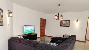 Un saló amb un televisor de pantalla plana gran, un sofà de color fosc, una taula de centre de vidre i una porta de fusta.