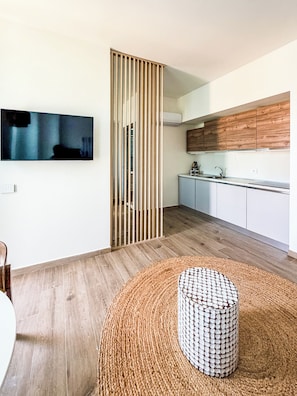 A modern kitchen with wooden cabinets, a built-in stove, and a dining area with a round woven ottoman. - La Casa di Betti (Portopalo di Capo Passero)