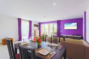 A dining area with a table set for two, a sofa, and a television on the wall.