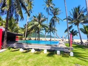 A pool area with lounge chairs, palm trees, and a beach view.