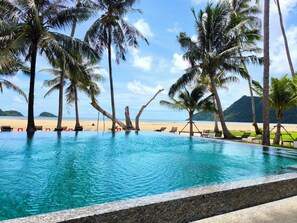 Una piscina con agua cristalina azul, rodeada de palmeras y vista a la playa.
