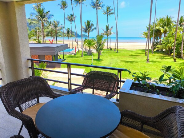 A balcony with wicker furniture, a pool, and a view of the beach and palm trees.