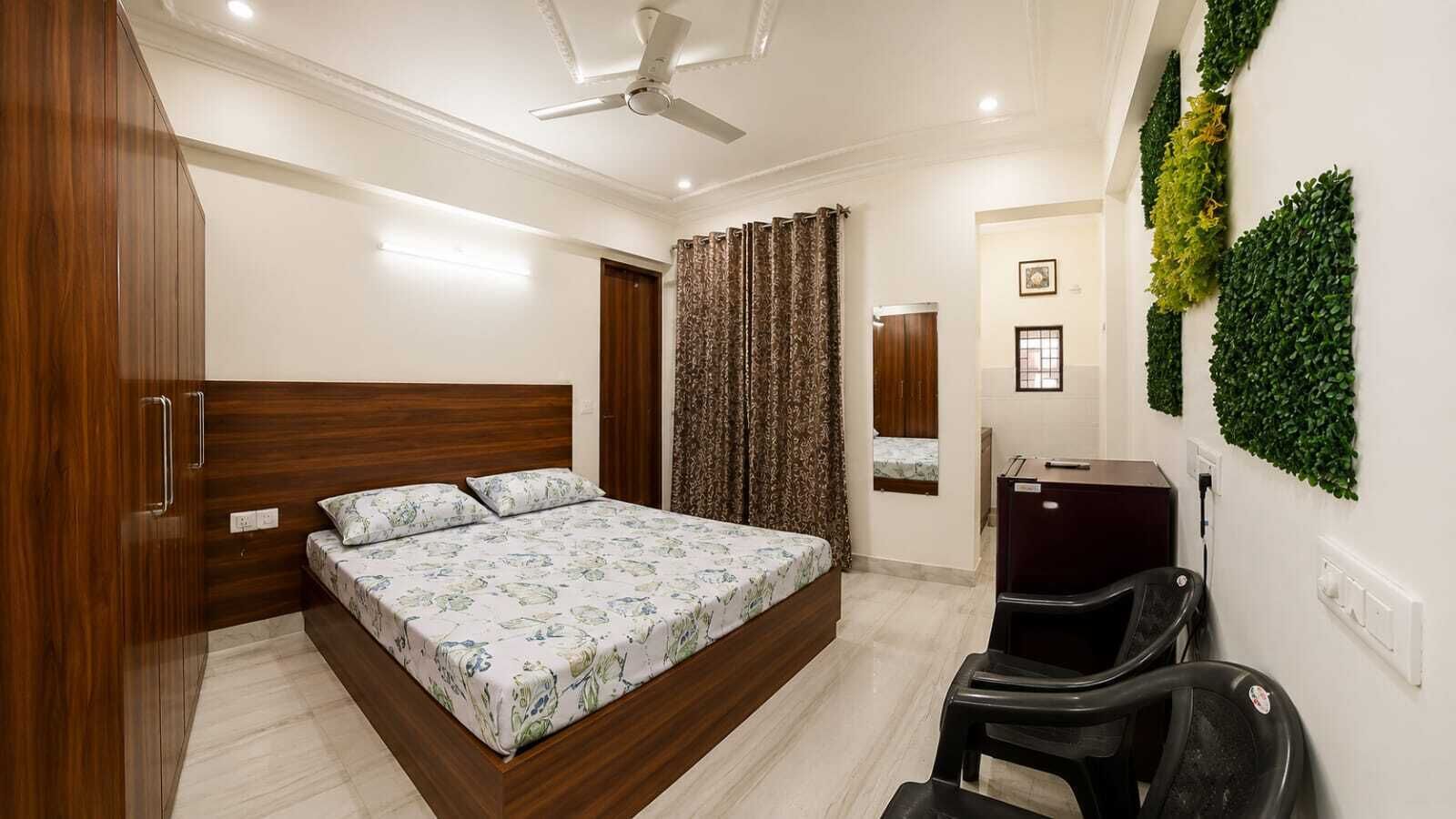 A bedroom with a bed, a wardrobe, a ceiling fan, a desk, and a wall-mounted green plant.