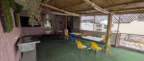 An outdoor patio area with tables and chairs, a grill, and a bamboo ceiling.