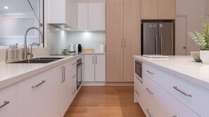 A modern kitchen with white cabinetry, stainless steel appliances, and a wooden floor. - Schuey's Shack | Luxury | Walk to Boomerang Beach (Boomerang Beach)