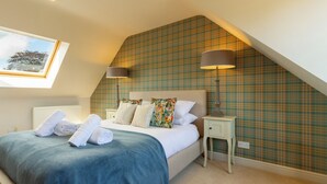 A bedroom with a sloped ceiling, a bed with a blue bedspread, two bedside lamps, and a plaid wallpaper. - Idyllic 1BDR Cottage on the Edge of Edinburgh (Edinburgh)