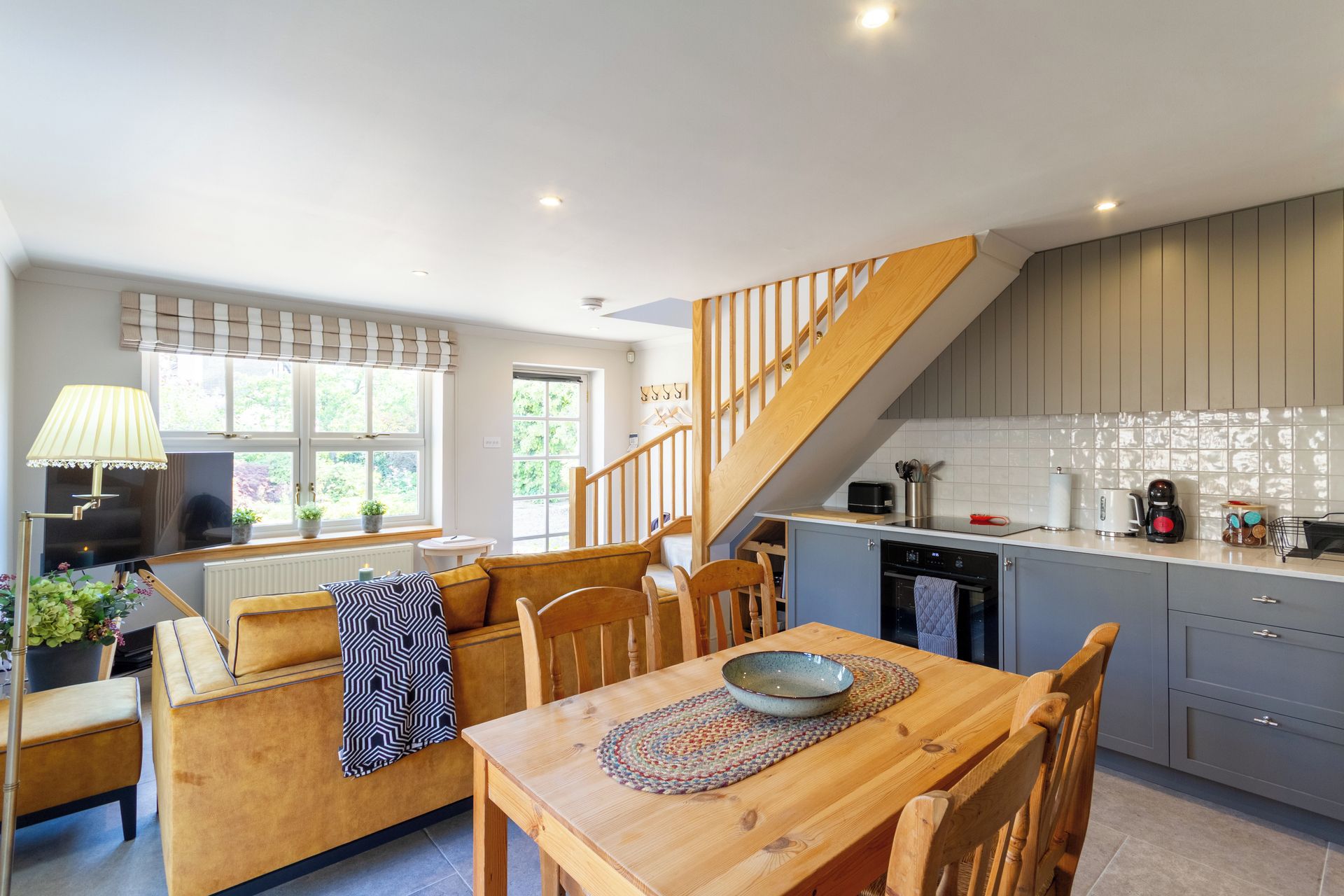 Une cuisine moderne avec un escalier en bois, un coin repas avec une table et des chaises, et un espace salon confortable avec un canapé et des coussins.