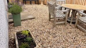 A patio area with a round wooden table and chairs, a black bench, and potted plants. - Idyllic 1BDR Cottage on the Edge of Edinburgh (Edinburgh)