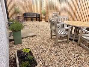 Eine Terrasse mit einem runden Holztisch und Stühlen, einer schwarzen Bank und Blumentöpfen.