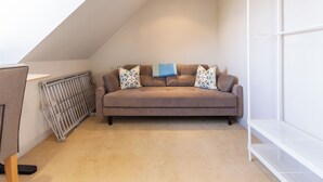 A cozy loft bedroom with a brown sofa, patterned cushions, a radiator, and a white shelving unit. - Idyllic 1BDR Cottage on the Edge of Edinburgh (Edinburgh)