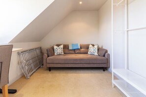 Ein gemütliches Schlafzimmer im Loft-Stil mit einem braunen Sofa, gemusterten Kissen, einer Heizung und einem weißen Bücherregal.