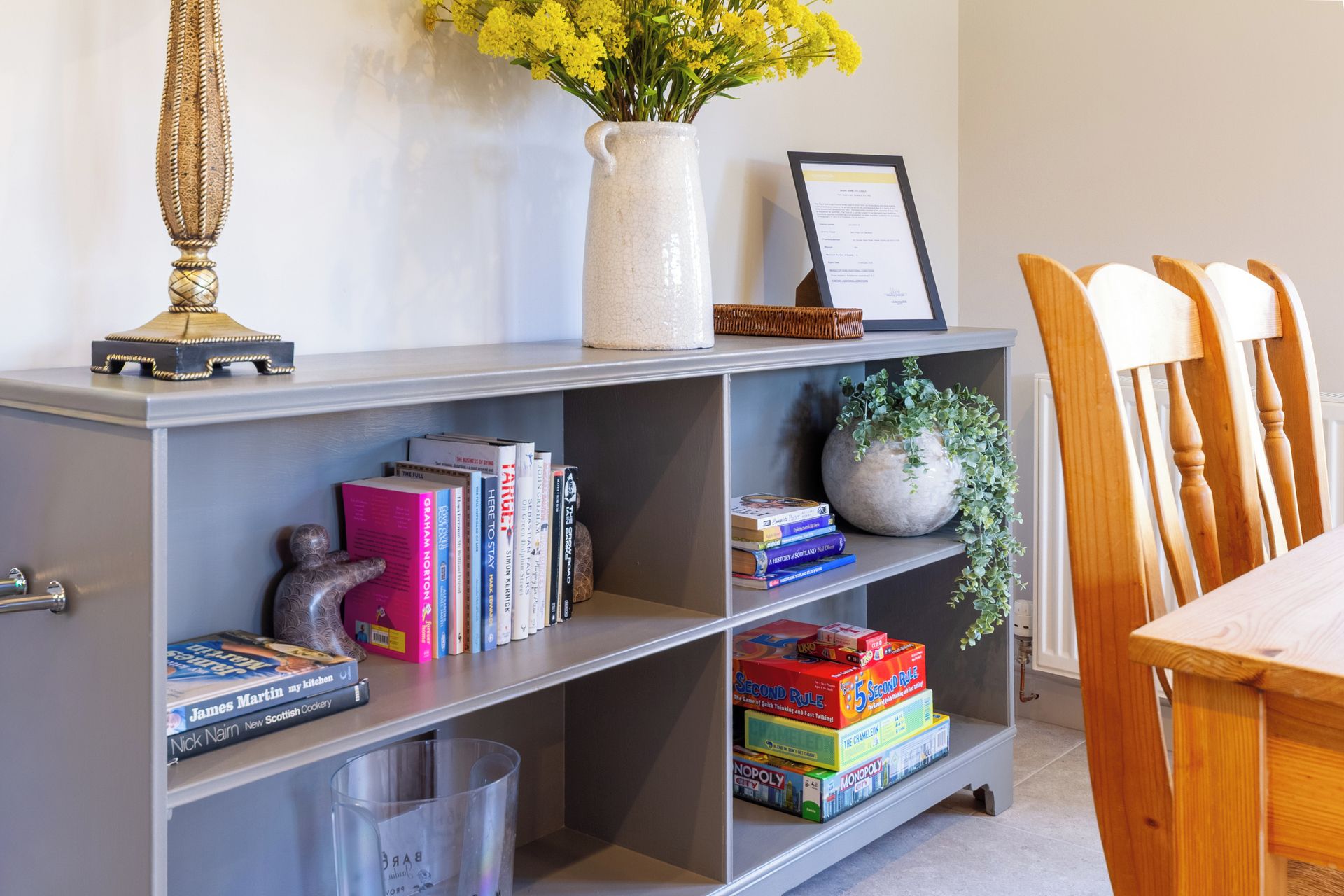 A bookshelf with books, a vase with flowers, a framed certificate, and a plant.