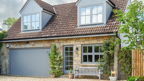A two-story house with a grey garage door, a stone facade, and a wooden fence. - Idyllic 1BDR Cottage on the Edge of Edinburgh (Edinburgh)