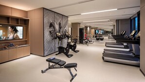 Een moderne sportschool met trainingsapparatuur, een televisie en een grote muur met abstracte kunst.