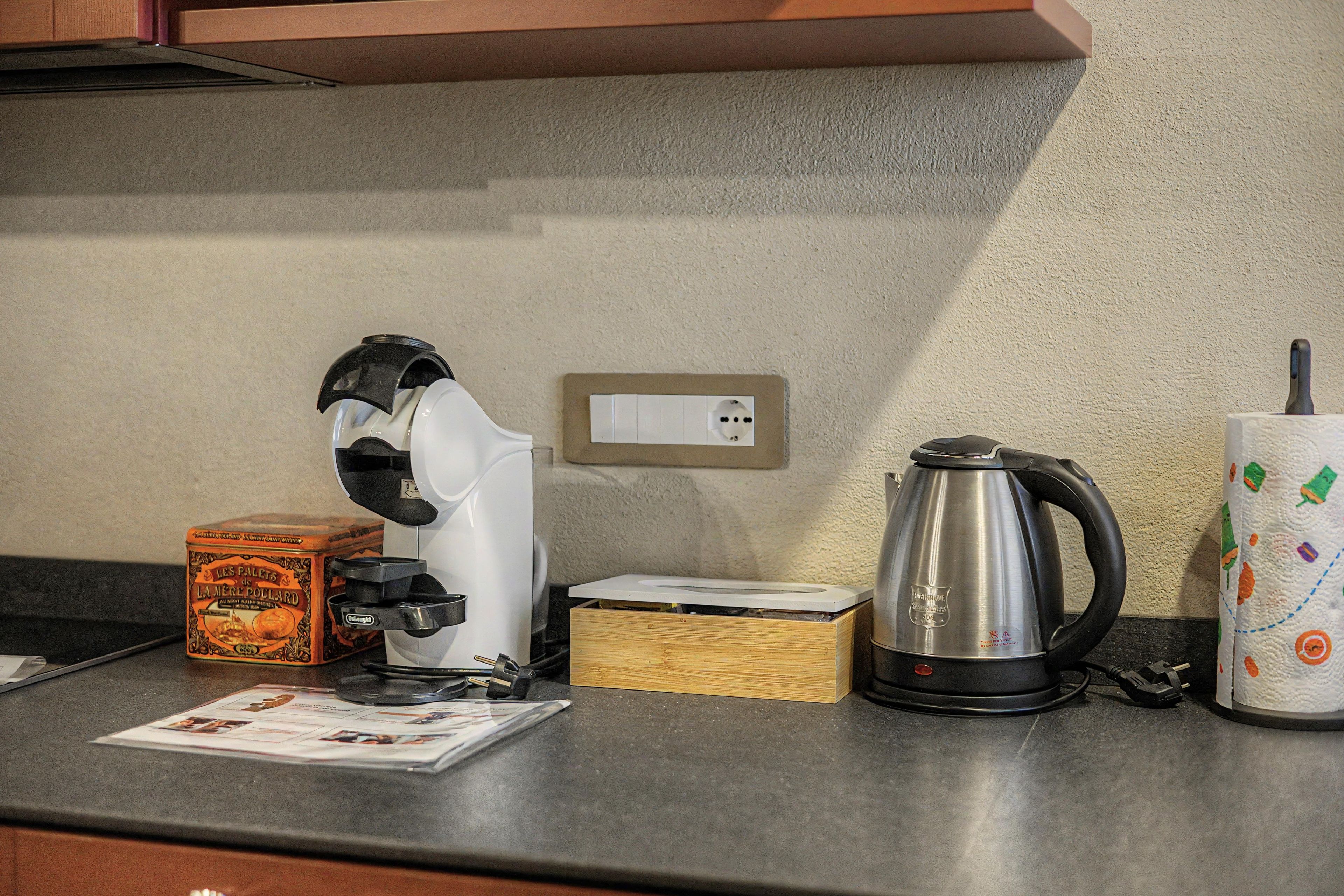 Un plan de travail de cuisine avec une machine à café, une bouilloire, une boîte et un journal.