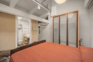 A bedroom with a bed, a wooden headboard, a wardrobe, and a bathroom with a bidet and towel rack.