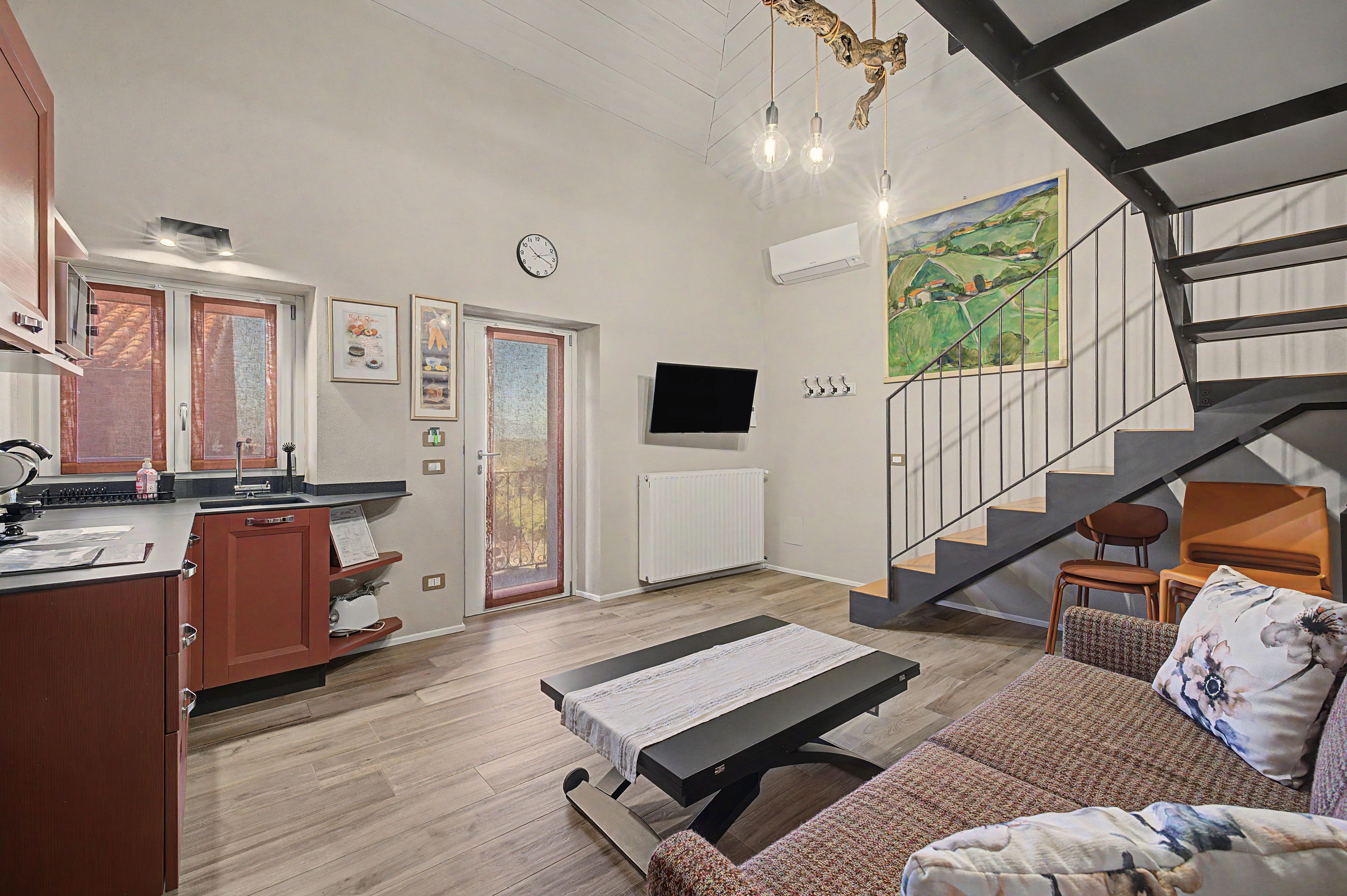 Eine moderne Küche mit Essbereich, einer Treppe und einem Wohnzimmer mit Sofa und Gemälde.