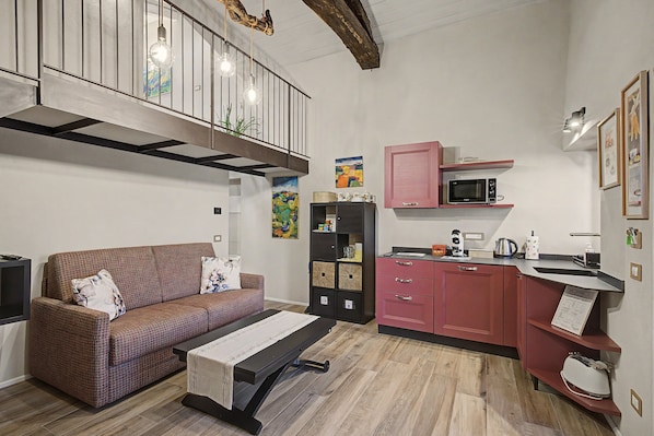 A compact living space with a sofa, a dining table, a kitchenette, and a staircase.