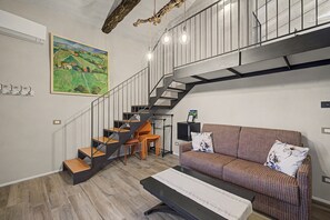 A modern interior with a staircase, a sofa, a dining table, and a painting on the wall.