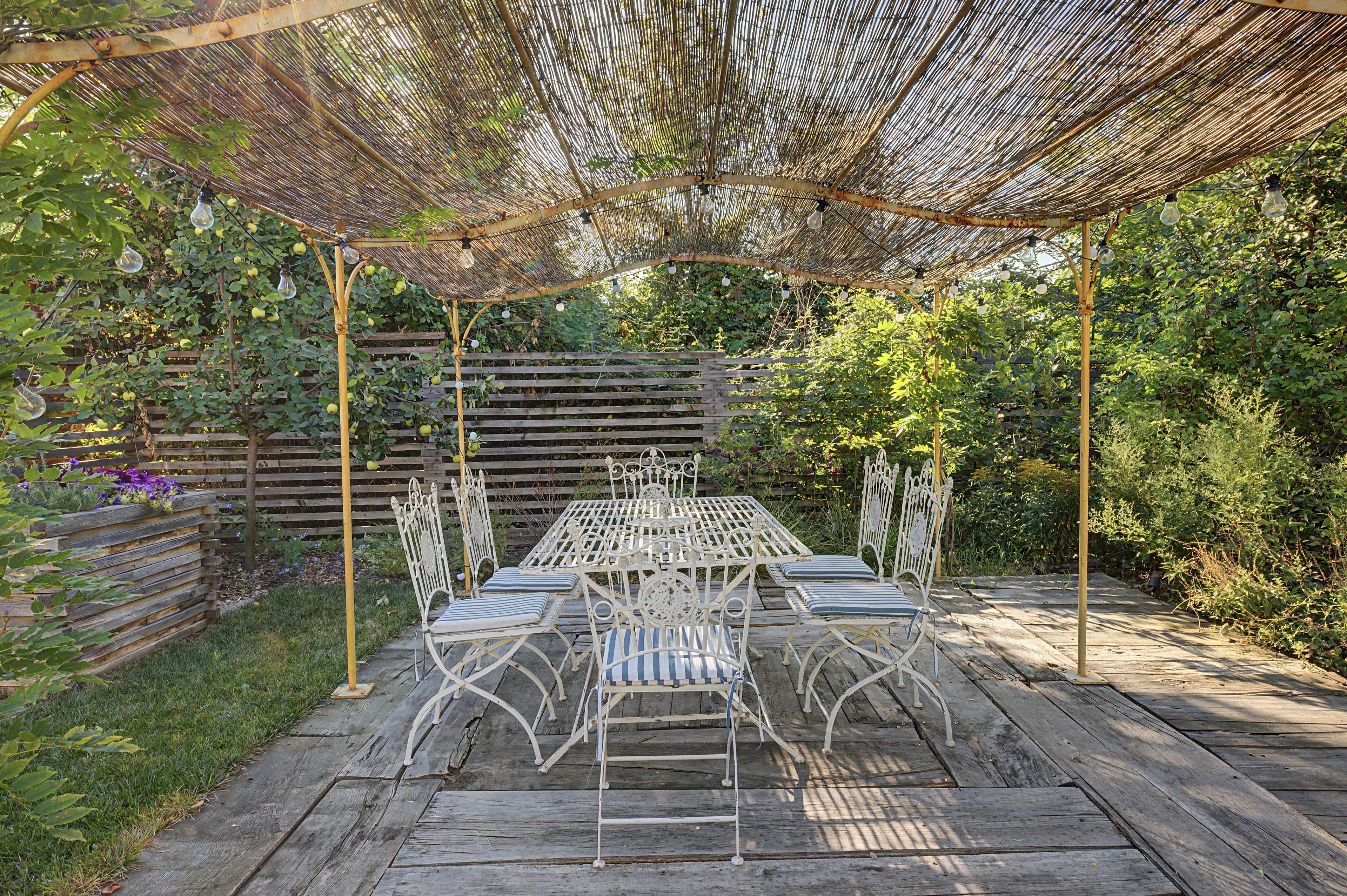 Eine Terrasse im Freien mit Tisch und Stühlen, umgeben von einem Holenzaun und viel Grün.