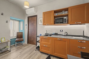 A compact kitchen with wooden cabinets, a microwave, a kettle, and a small sink.