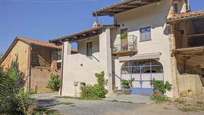 A two-story building with a balcony, a large arched window, and a gravel driveway. - Accessible "Terre" Apartment near Garden with Wi-Fi and Air Conditioning (Dogliani)
