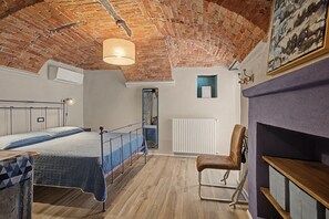 A room with a bed, a chair, a radiator, and a ceiling with exposed brick.