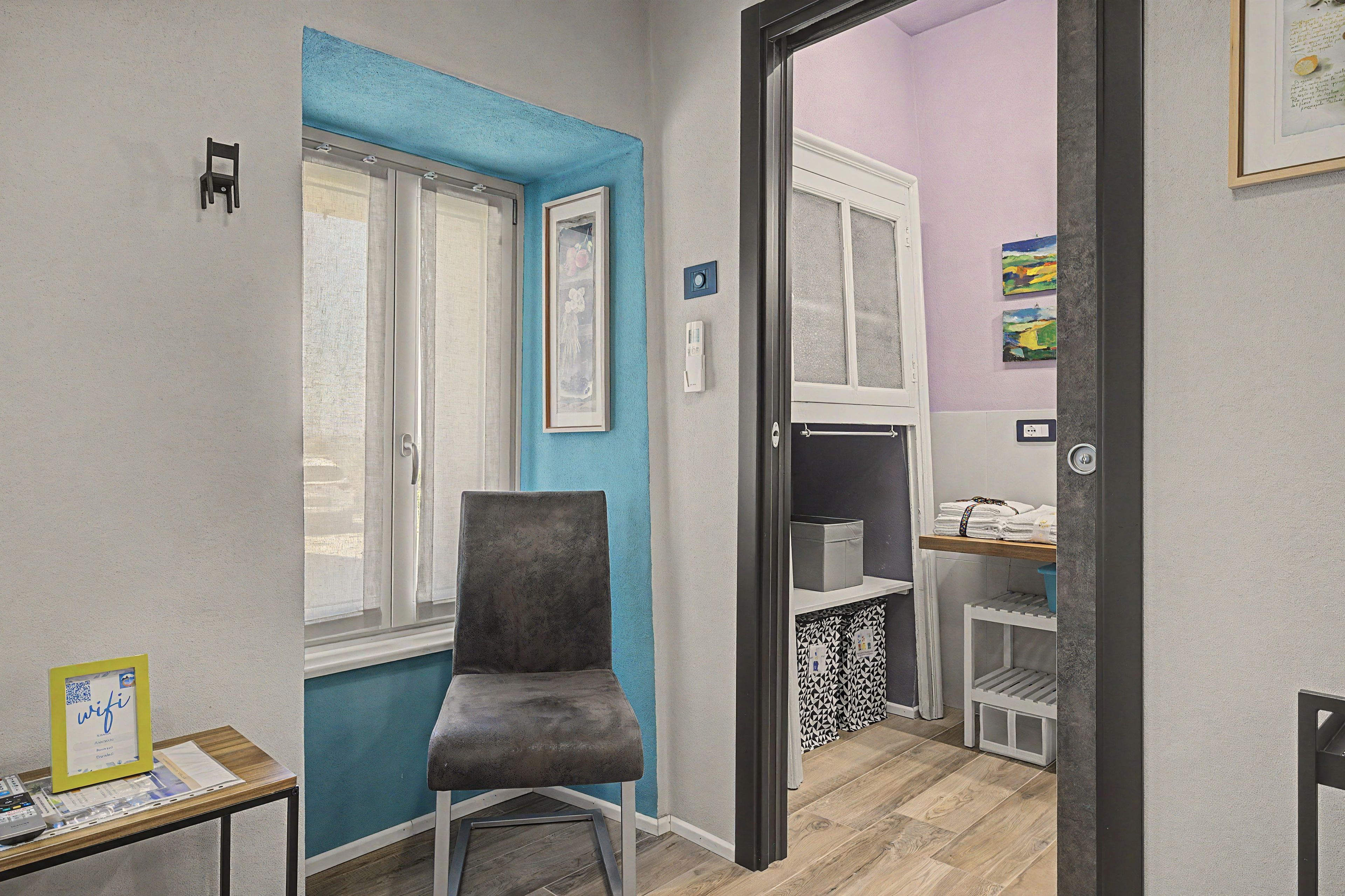 Ein Zimmer mit Fenster, einem Stuhl, einem Regal mit Handtüchern und einer Tür zu einem anderen Raum.