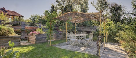 A wooden deck with outdoor furniture, a pergola with string lights, and a garden with various plants.