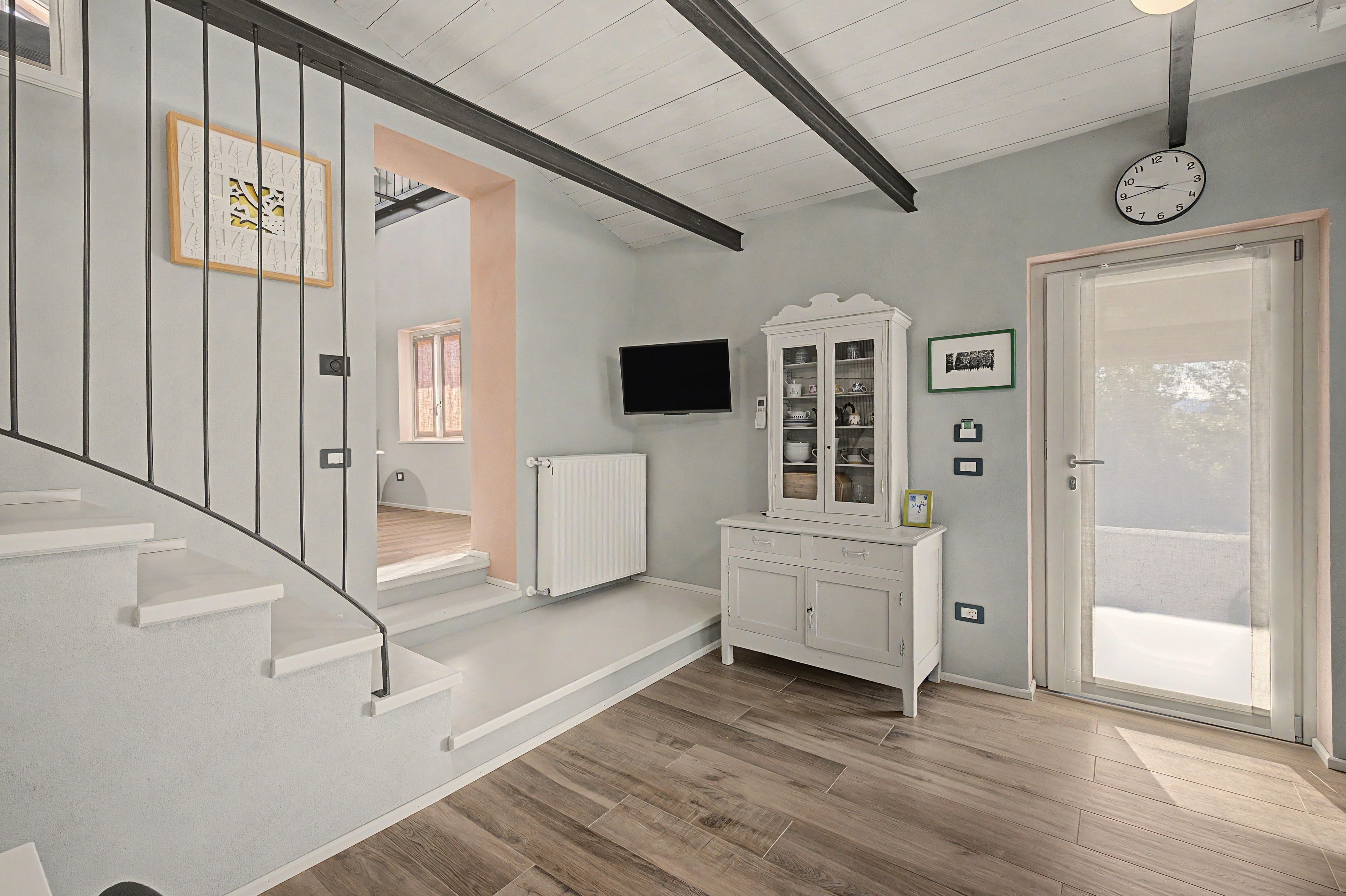 Un escalier au design moderne, un radiateur blanc, un téléviseur fixé au mur et une porte dotée d’un panneau en verre.