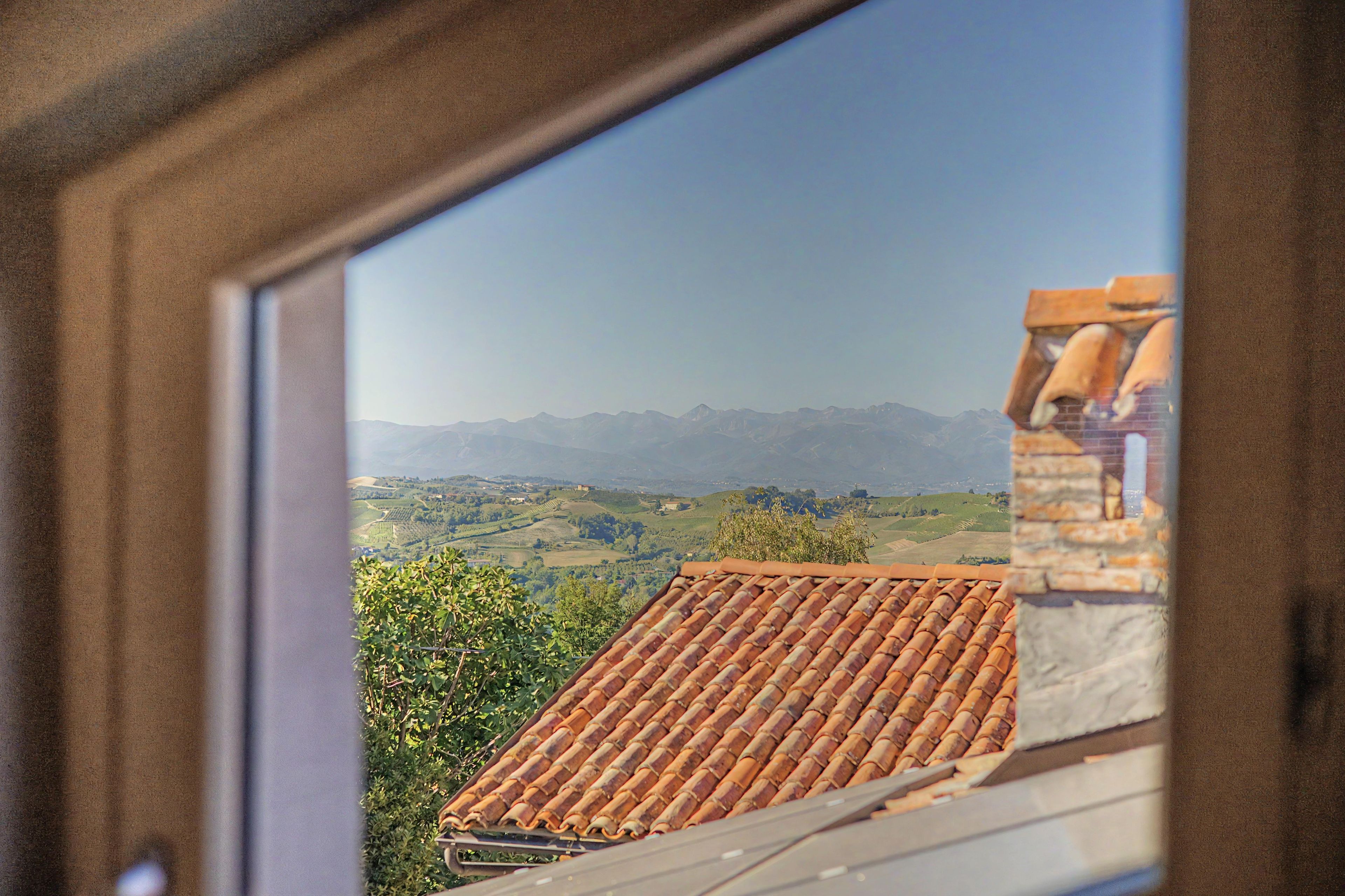 Vista pela janela de uma paisagem montanhosa com telhas de barro e vegetação.