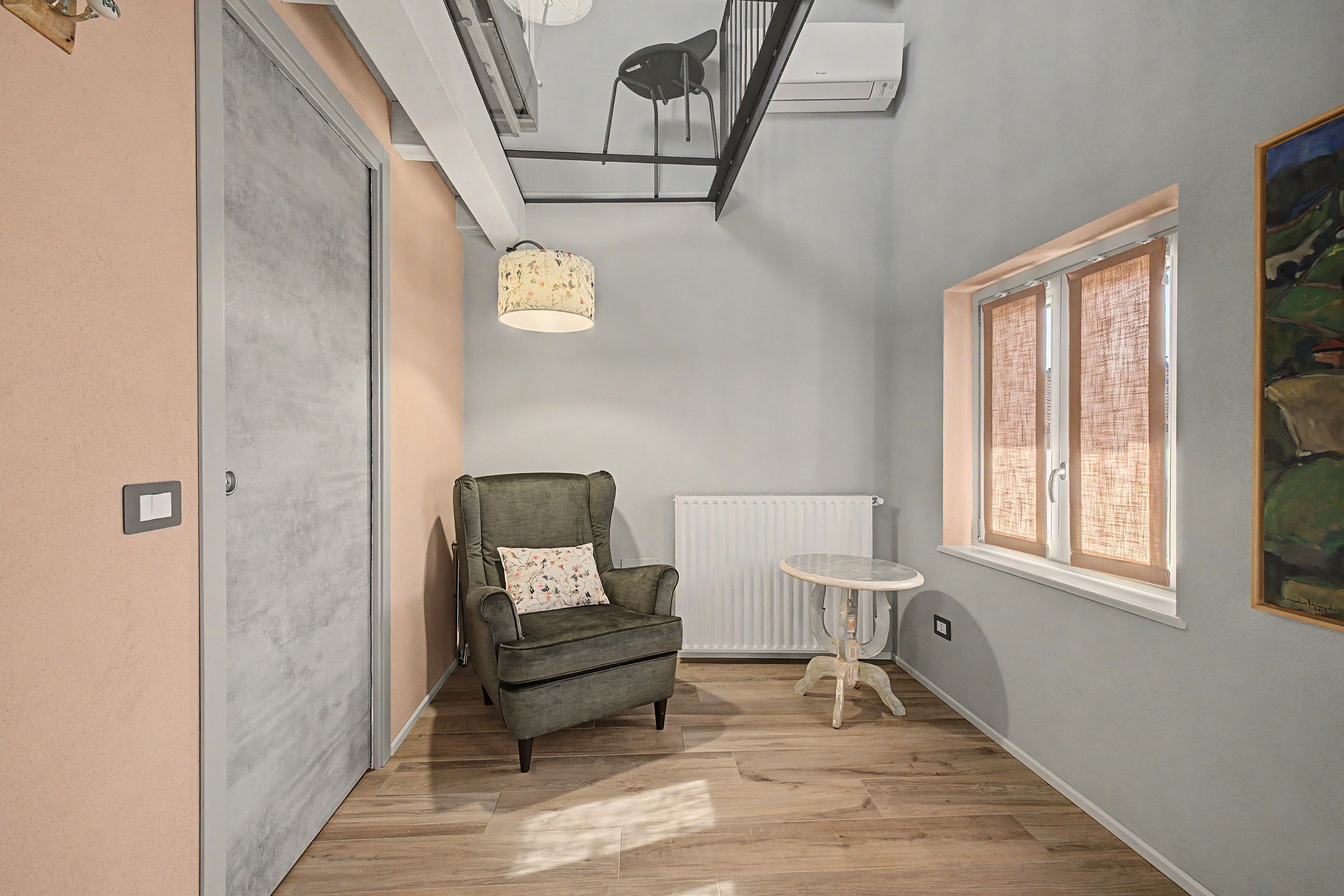 A room with a grey armchair, a small round table, a radiator, and a window with blinds.