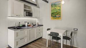 Eine kompakte Küchenzeile mit Mikrowelle, Spüle und Stauraumschränken. Es ist ein kleiner Esstisch mit zwei Stühlen und ein Bild an der Wand vorhanden.